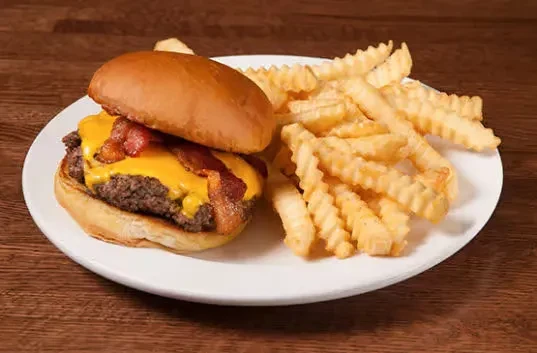 Cheeseburger with bacon, melted cheese, and crinkle-cut fries on a white plate.