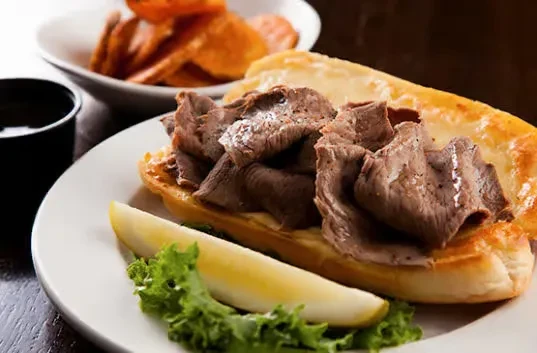 Close-up of a roast beef sandwich, pickle, and fries on a plate.