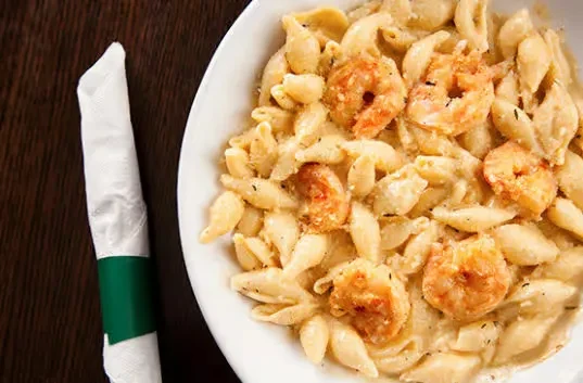 Creamy shell pasta with shrimp and herbs in a white bowl.