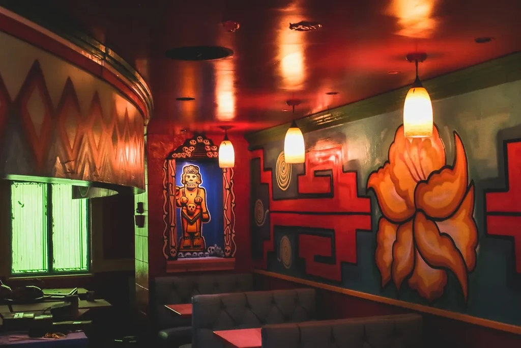 Restaurant interior with colorful murals, skull art, and red reflective ceiling.