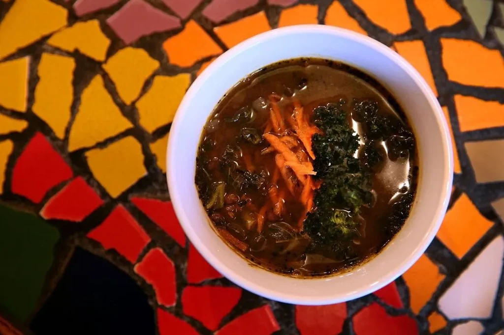 Dark soup with carrots and greens in white bowl on mosaic.