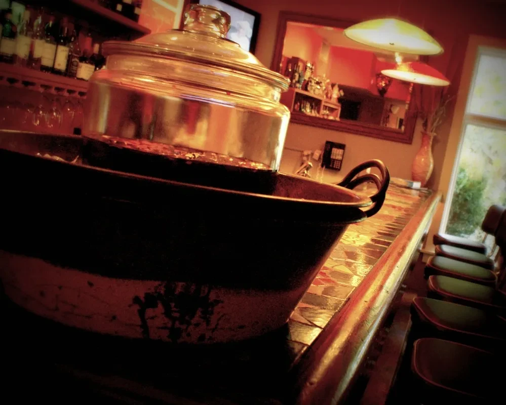 Dark serving pot on a reddish tiled bar counter with bottles.