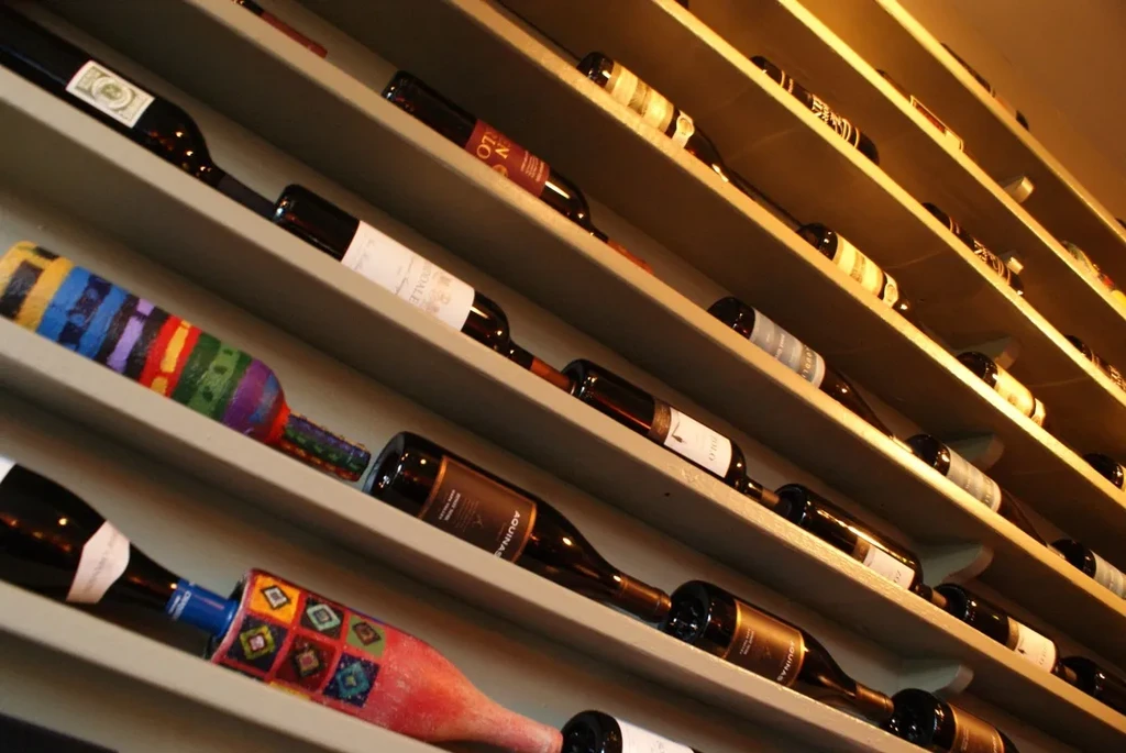 Wall-mounted wine rack filled with numerous bottles, two artistically decorated.