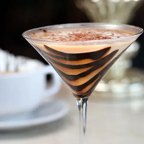 Martini glass with creamy layered drink, chocolate stripes, and powder.