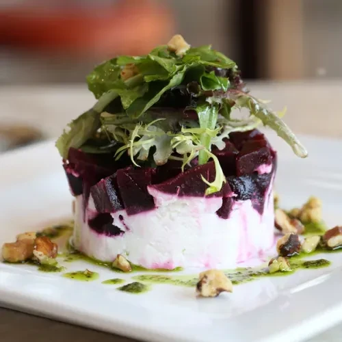 Layered stack of cheese, beets, greens, nuts, and green oil.