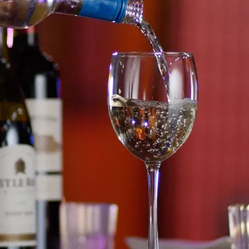 White wine pours from a blue-capped bottle into a clear glass.