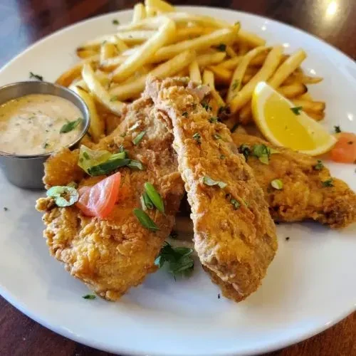 Close-up of golden-brown fish and chips, lemon, and dipping sauce.