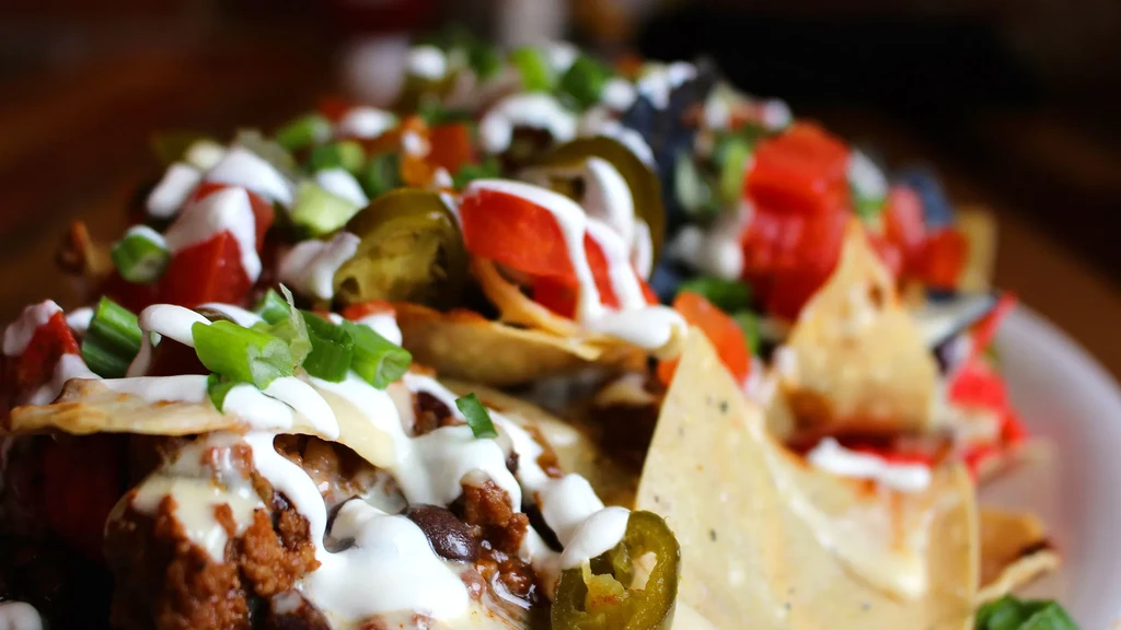 Plate of loaded nachos with meat, melted cheese, sour cream, and veggies.