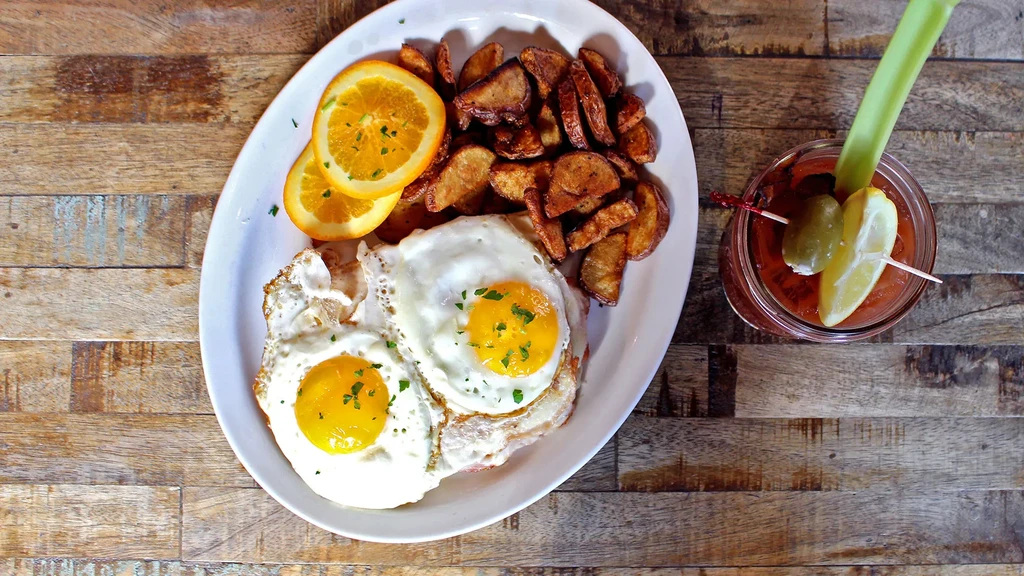 Overhead: Fried eggs, potato wedges, orange slices, and a Bloody Mary.