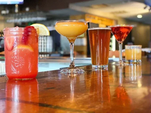 Close-up of five alcoholic drinks in various glasses on a bar.