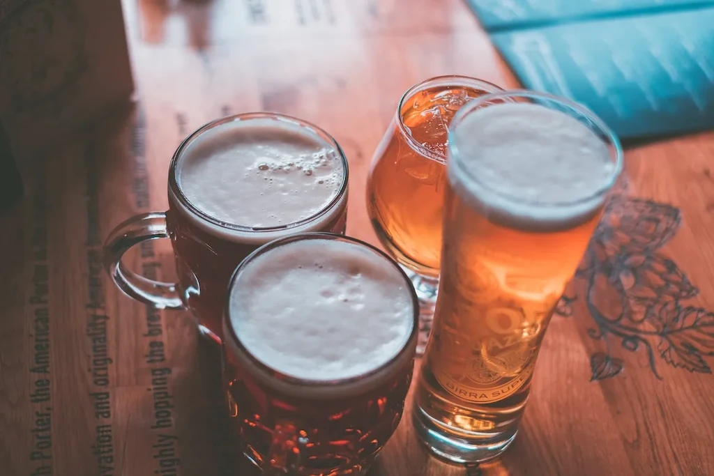 Four glasses of different beers on a wooden table with engravings.