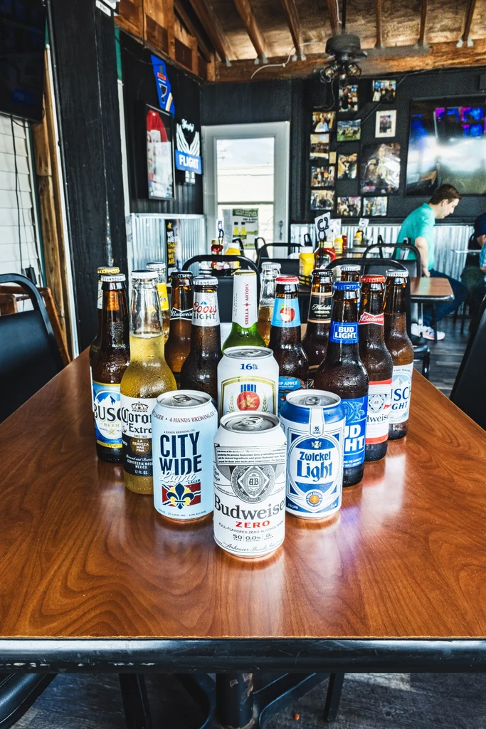 Assortment of cold beer bottles and cans with condensation in a bar.