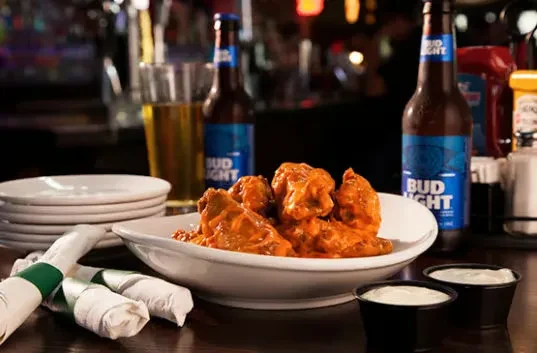 Reddish-orange buffalo wings, dipping sauce, and beer at a bar.