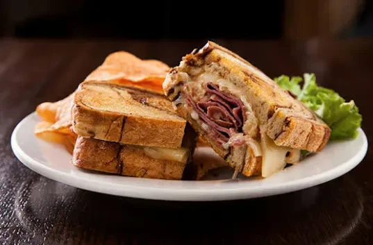 Grilled deli meat and cheese sandwich with chips and lettuce.