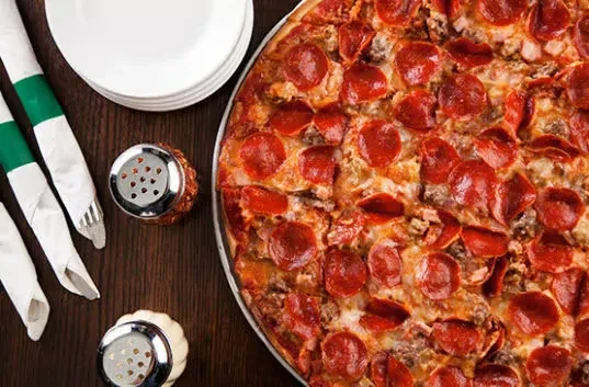 Freshly baked pepperoni pizza in pan, with plates and shakers.