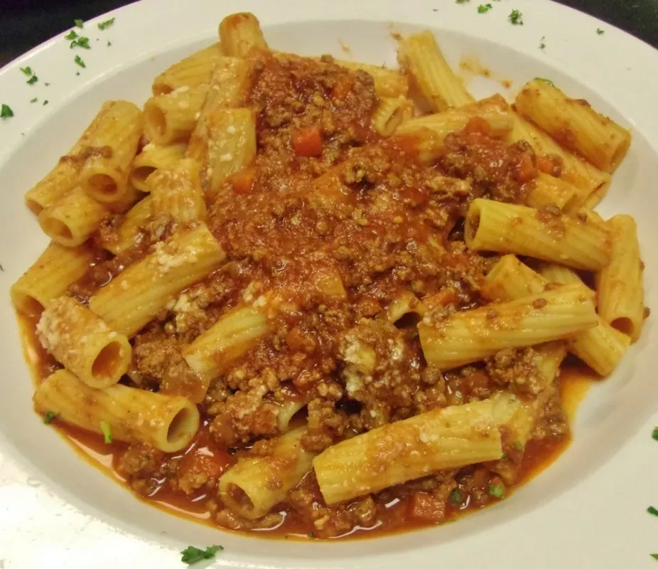 Rigatoni pasta with chunky meat sauce, grated cheese, and green herbs.