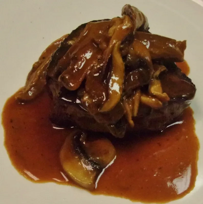 Dark meat with sautéed mushrooms and rich sauce on a white plate.