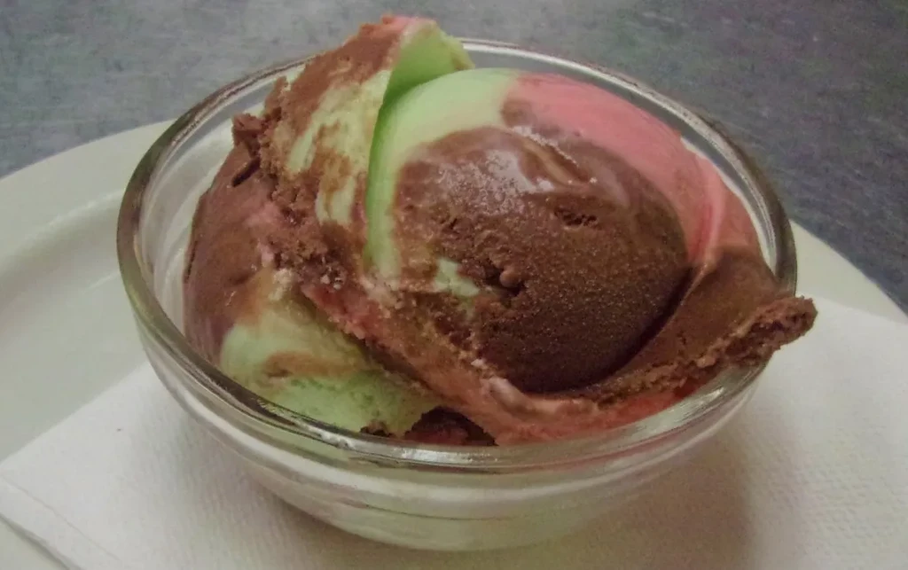 Multi-flavored ice cream swirled in a glass bowl with a napkin.