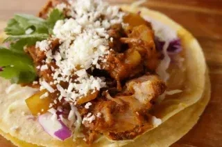 Vibrant corn taco with shredded meat, cotija cheese, cilantro, and cabbage.