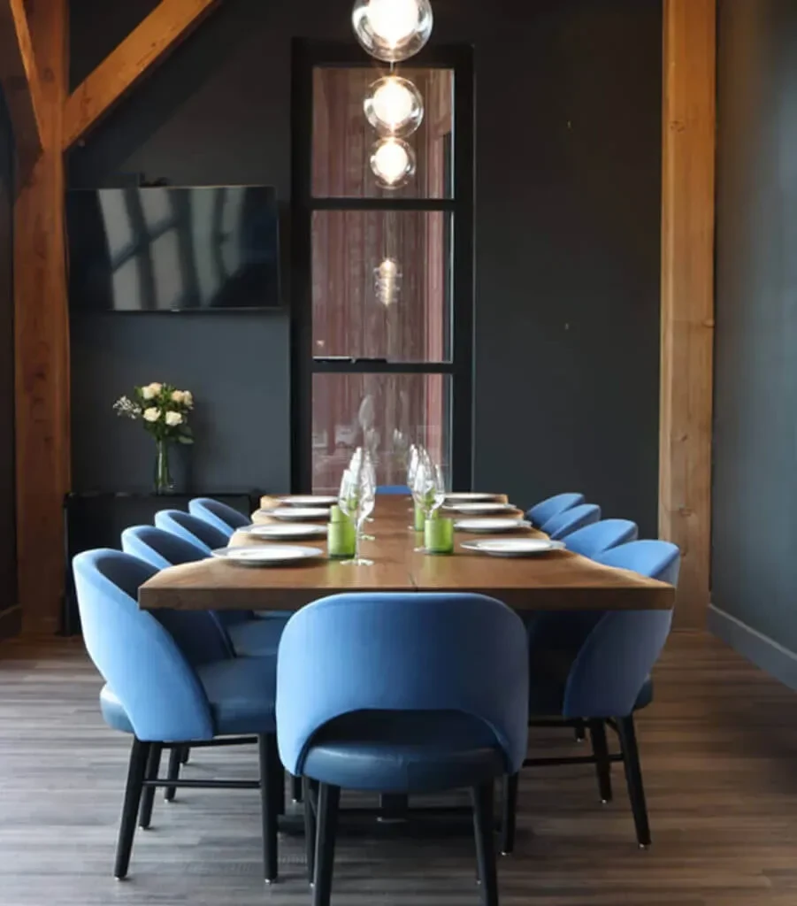Modern dining room with long wooden table, blue chairs, and pendant lights.