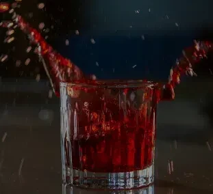 Red liquid dramatically splashing from a ribbed glass against a dark background.