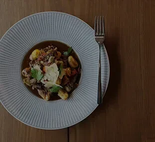 Dimly lit plate of gnocchi and meat stew with cheese, fork.