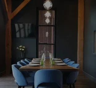 Long wooden dining table with blue chairs in a dark, beamed room.