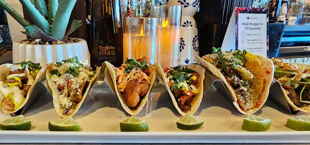 Six diverse tacos on platter, with Don Julio and charity sign.
