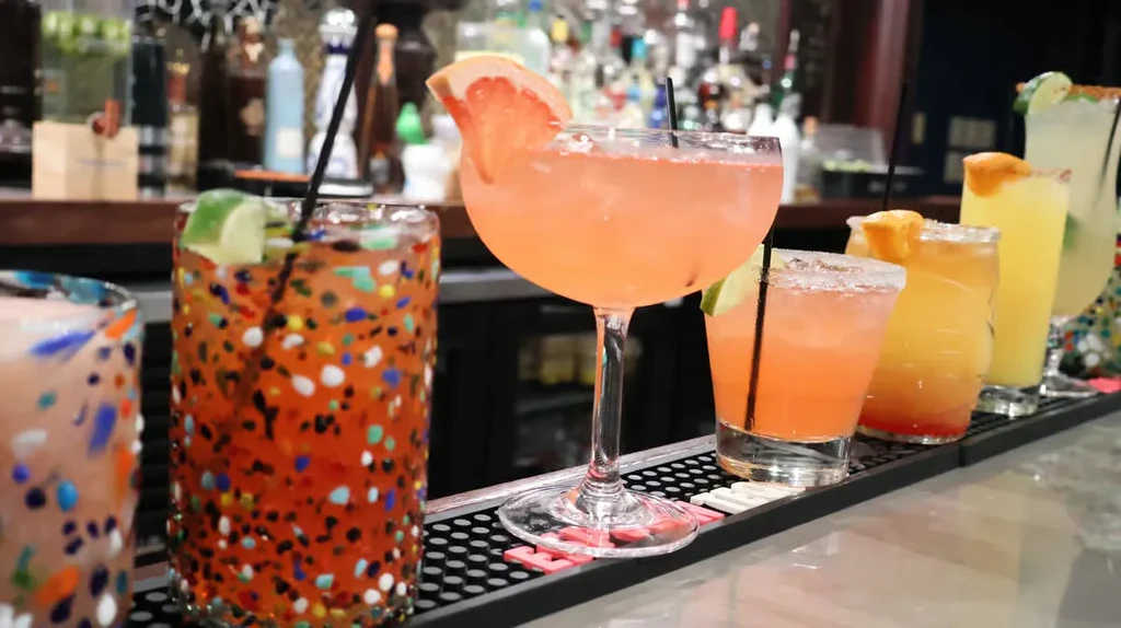Colorful cocktails with garnishes displayed on a well-stocked bar.