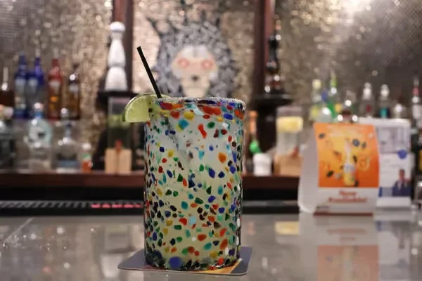 Colorful cocktail in a confetti glass with lime on a bar.