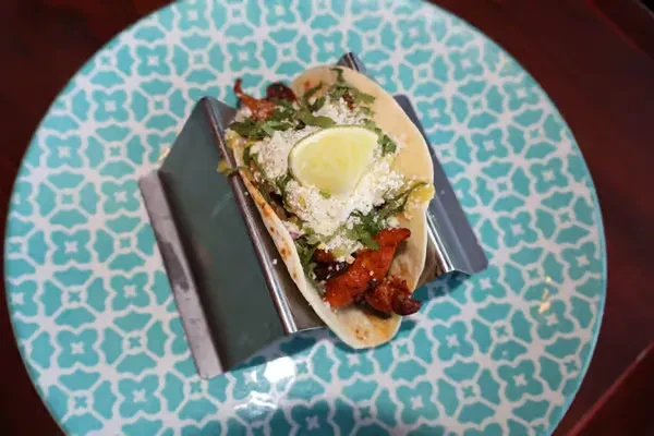 Taco with meat, cheese, cilantro, and lime wedge on a teal plate.