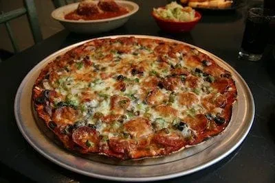 Deep-dish pizza with pepperoni, green peppers, and olives, served with sides.