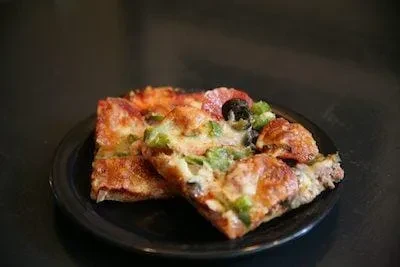 Two thick-crust pizza slices with pepperoni, olives, and green peppers.