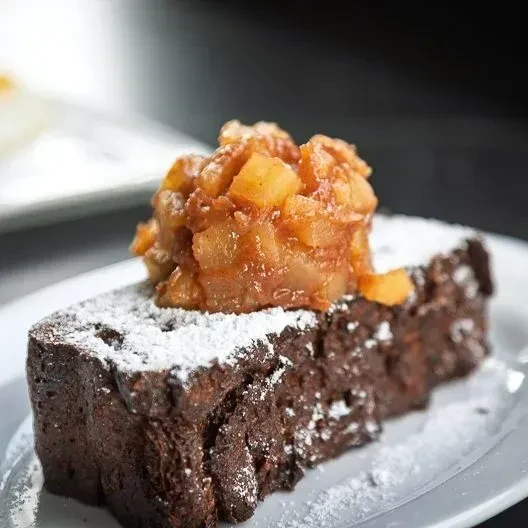 Slice of dark cake topped with powdered sugar and caramelized apples.