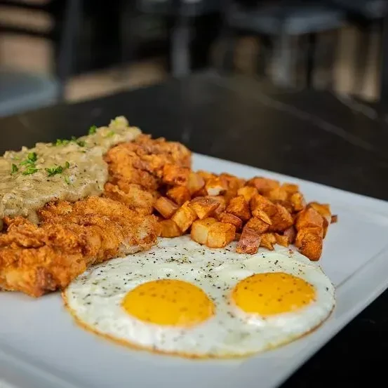Fried chicken with gravy, roasted potatoes, and sunny-side-up eggs.
