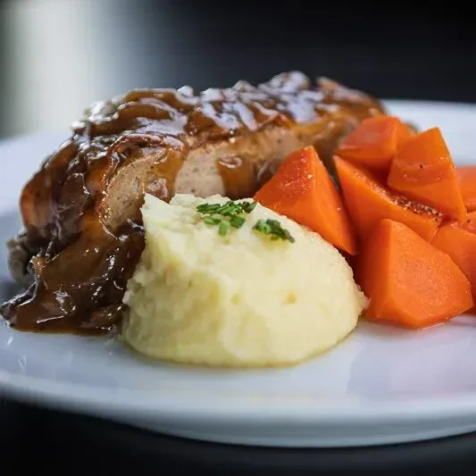 Meal with gravy-coated meat, mashed potatoes, and carrots.
