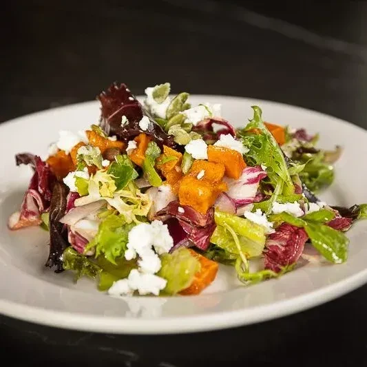 Colorful salad with mixed greens, orange squash, feta, and pepitas.