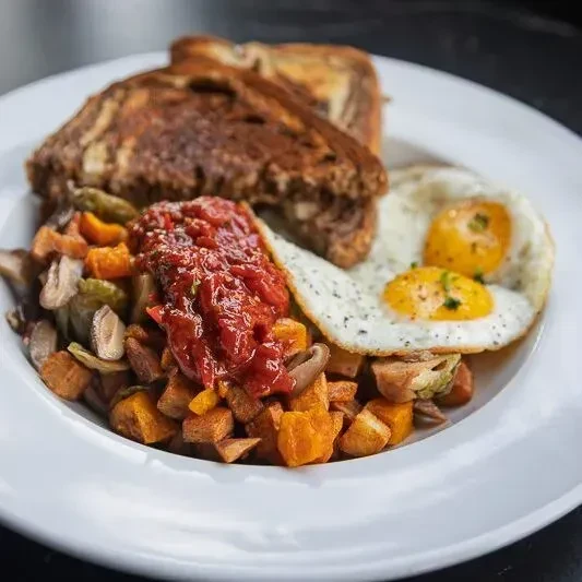 Sunny-side-up eggs, vegetable hash with red sauce, and toast.