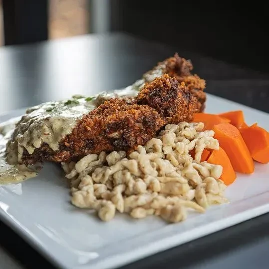 Crispy fried cutlets, creamy sauce, spaetzle, and carrots on a plate.