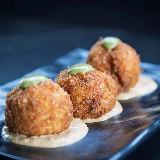 Three crispy golden-brown appetizers with two sauces on a dark plate.