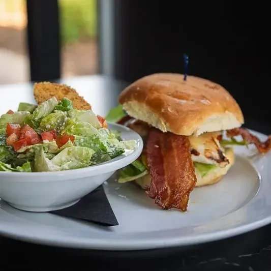 Chicken sandwich with bacon, lettuce, and a green side salad.