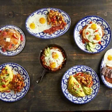 Six plates of varied breakfast foods on a rustic wooden table.