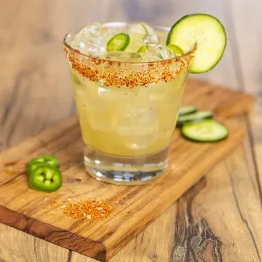 Cocktail with jalapeño, cucumber, and spiced rim on a wooden board.