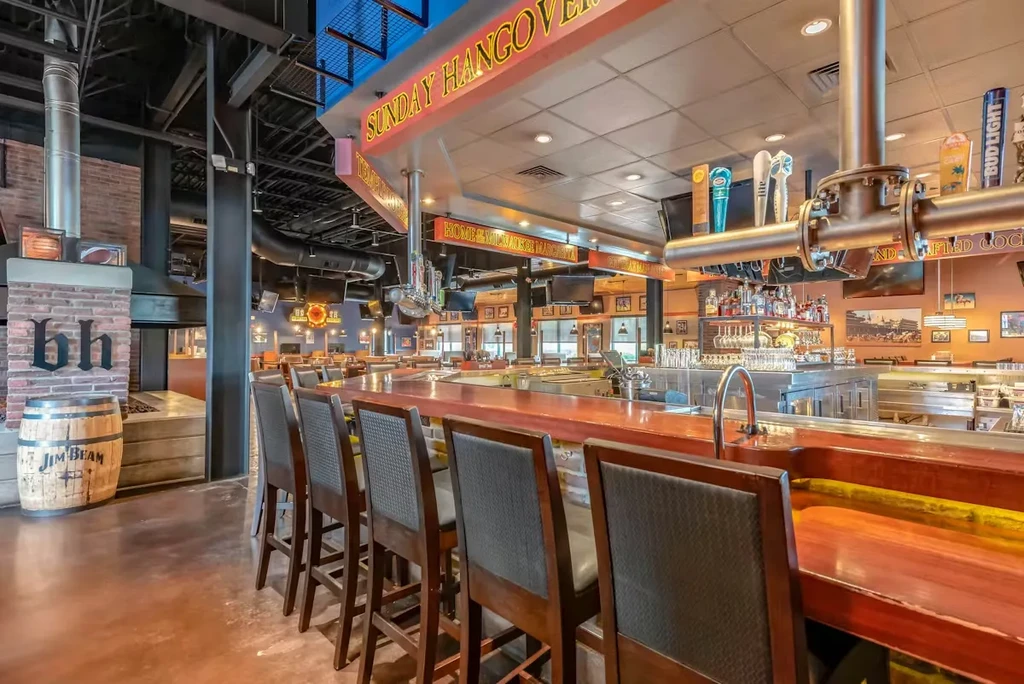 Industrial bar with a wooden counter, beer taps, neon signs, and fireplace.