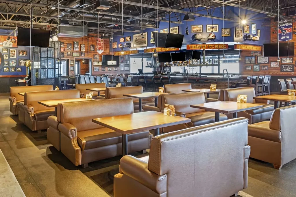 Spacious, empty sports bar with booths, long bar, TVs, and memorabilia.