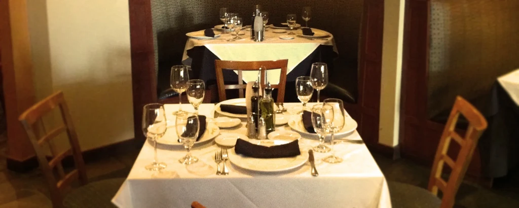 Dimly lit restaurant interior shows two empty dining tables meticulously set.