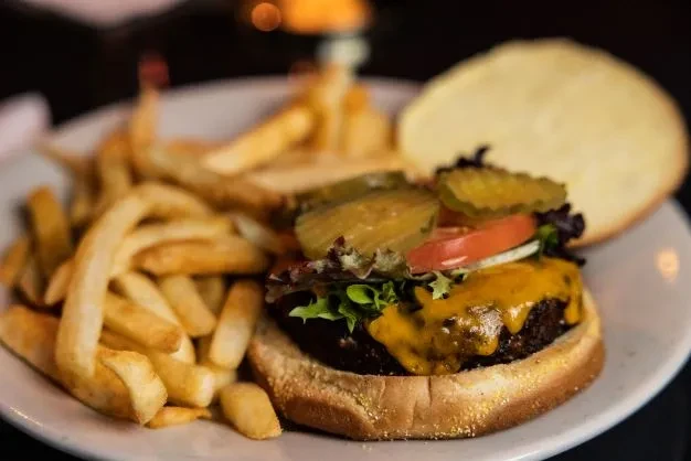 Open-faced cheeseburger with melted cheese, lettuce, tomato, pickles, and fries.
