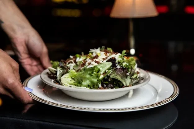 Close-up of vibrant salad with cheese and bacon, held by server's hands.