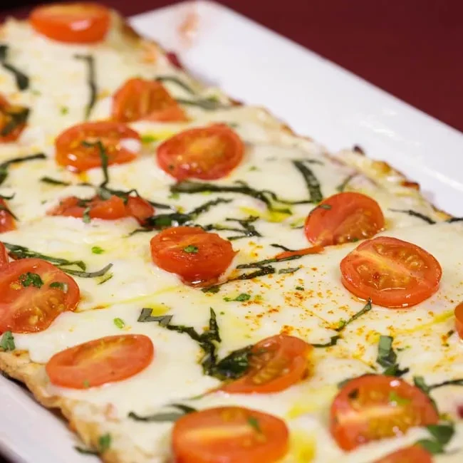 Focaccia-style flatbread with melted cheese, halved tomatoes, basil, and red spice.