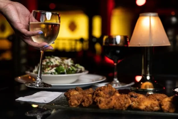 Dimly lit table with fried food, salad, and wines, hand holding one.